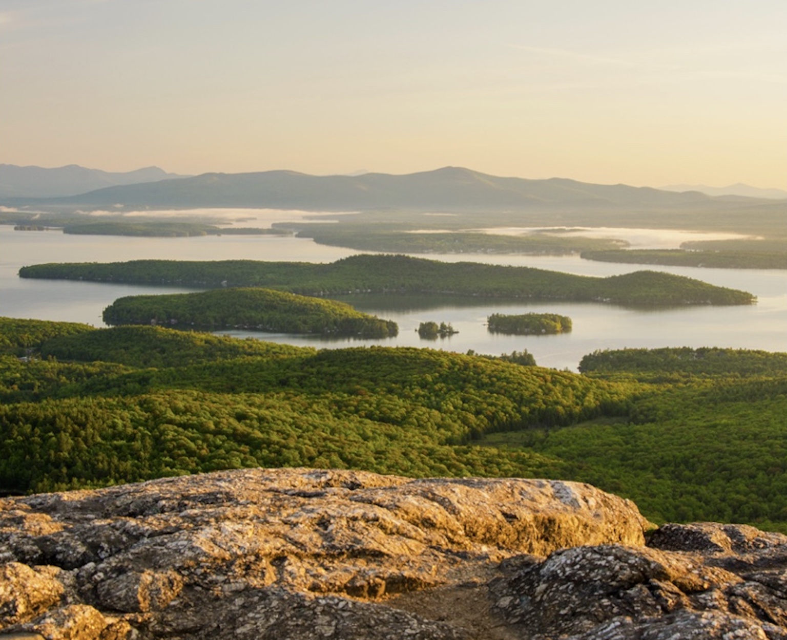 Sunrise over the lake and hills from a rock outcrop.
